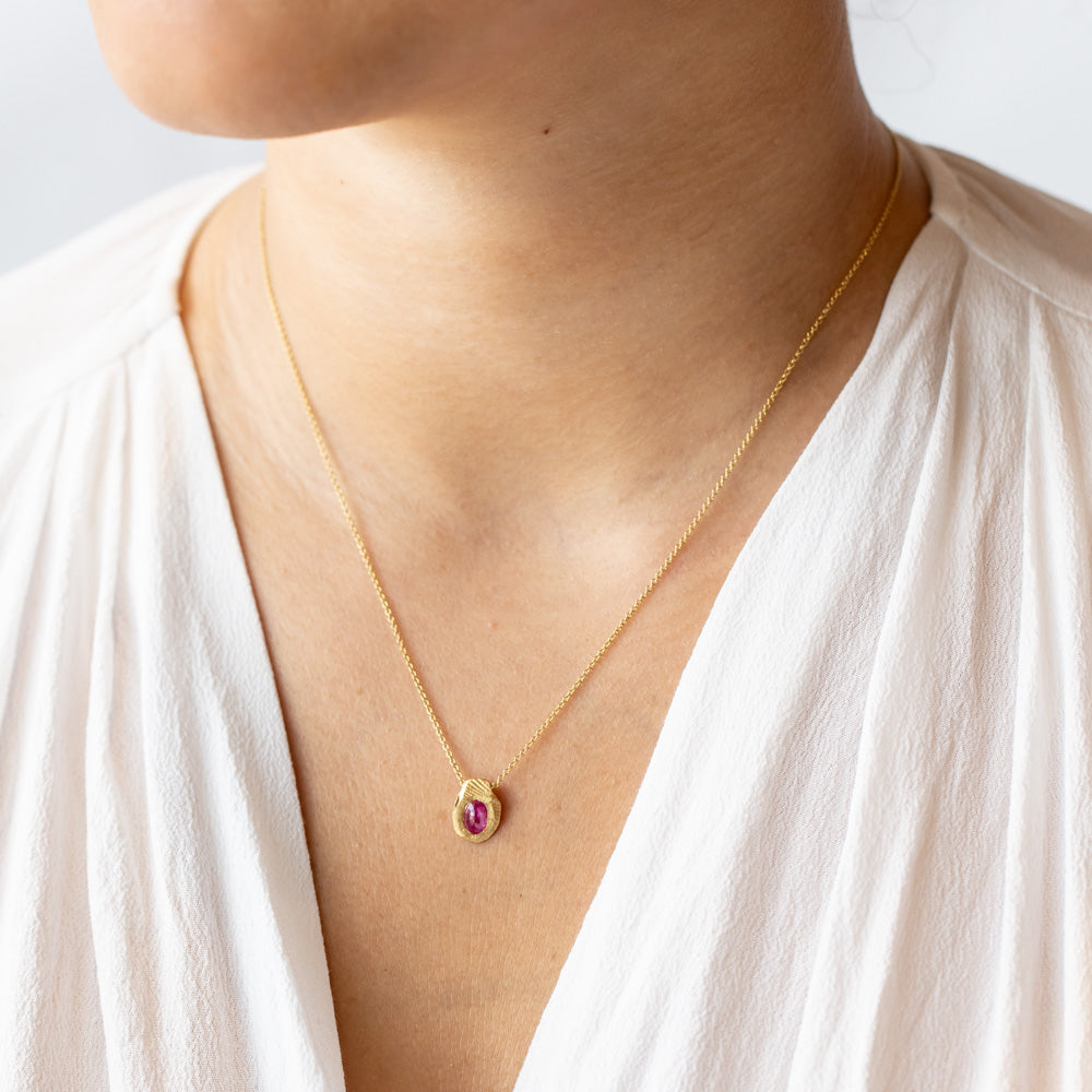 On oval ruby set into a carved yellow gold slider pendant on a classic cable chain necklace. On model.