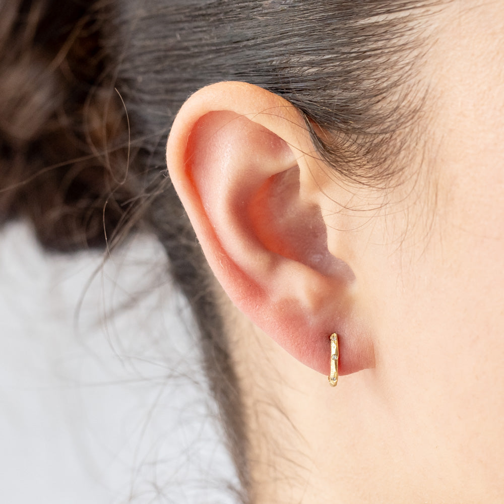 Small, textured yellow gold hoop earrings with three small diamonds along the front. On model.