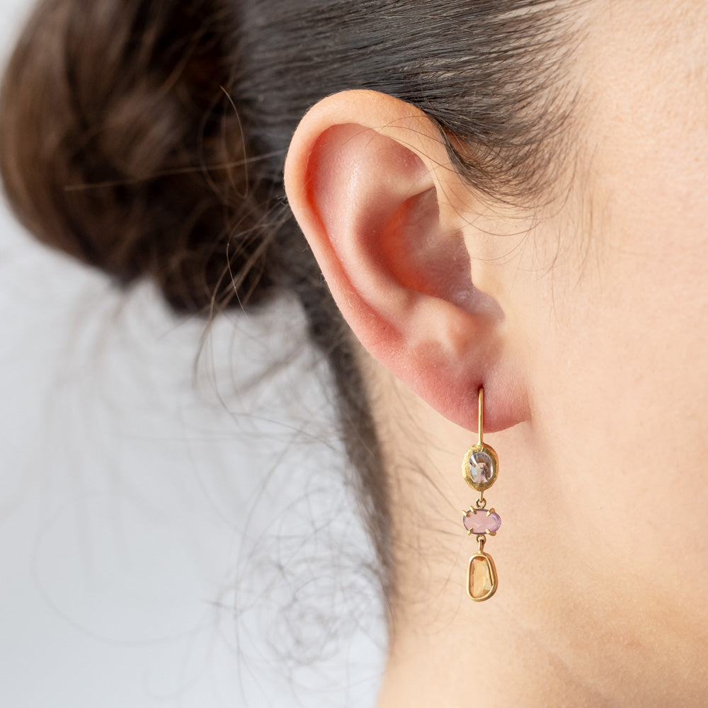 A pair of drop earrings featuring different colored freeform cut sapphires set in different ways in yellow gold. On model.