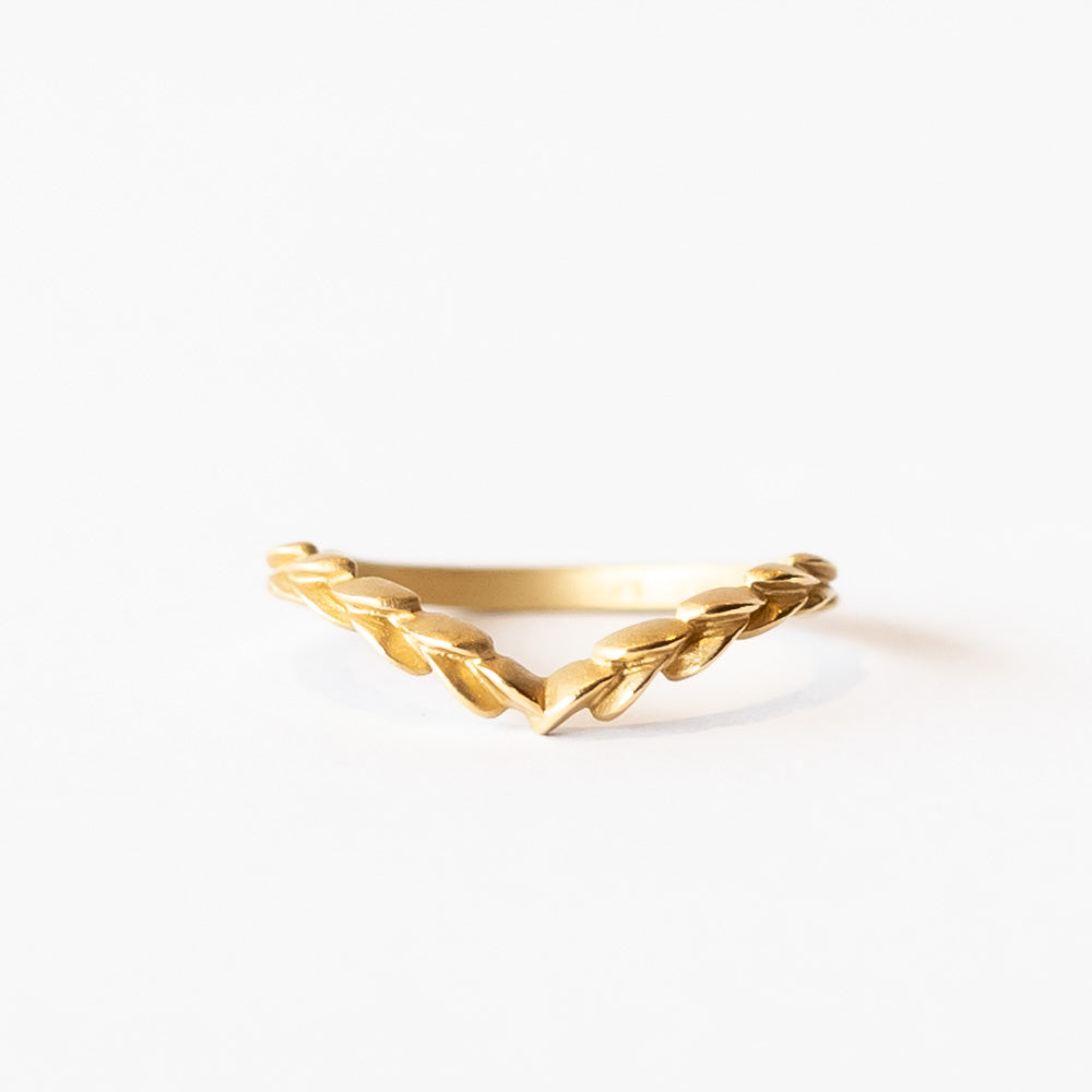 A yellow gold, matte finished contour wedding band that comes to a point, adorned with carved laurel pattern on the top.