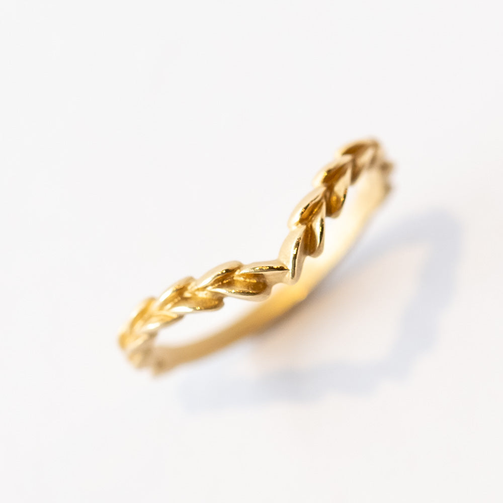 A yellow gold, matte finished contour wedding band that comes to a point, adorned with carved laurel pattern on the top.
