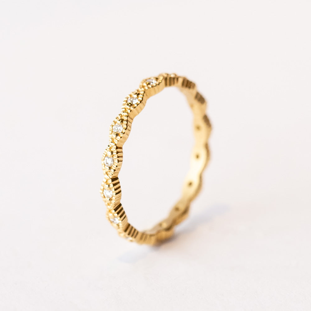 A yellow gold diamond eternity band with diamond shaped pattern all the way around, each shape is set with a small round diamond with milgrain bead edges.