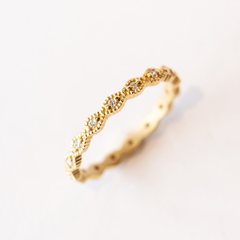 A yellow gold diamond eternity band with diamond shaped pattern all the way around, each shape is set with a small round diamond with milgrain bead edges.