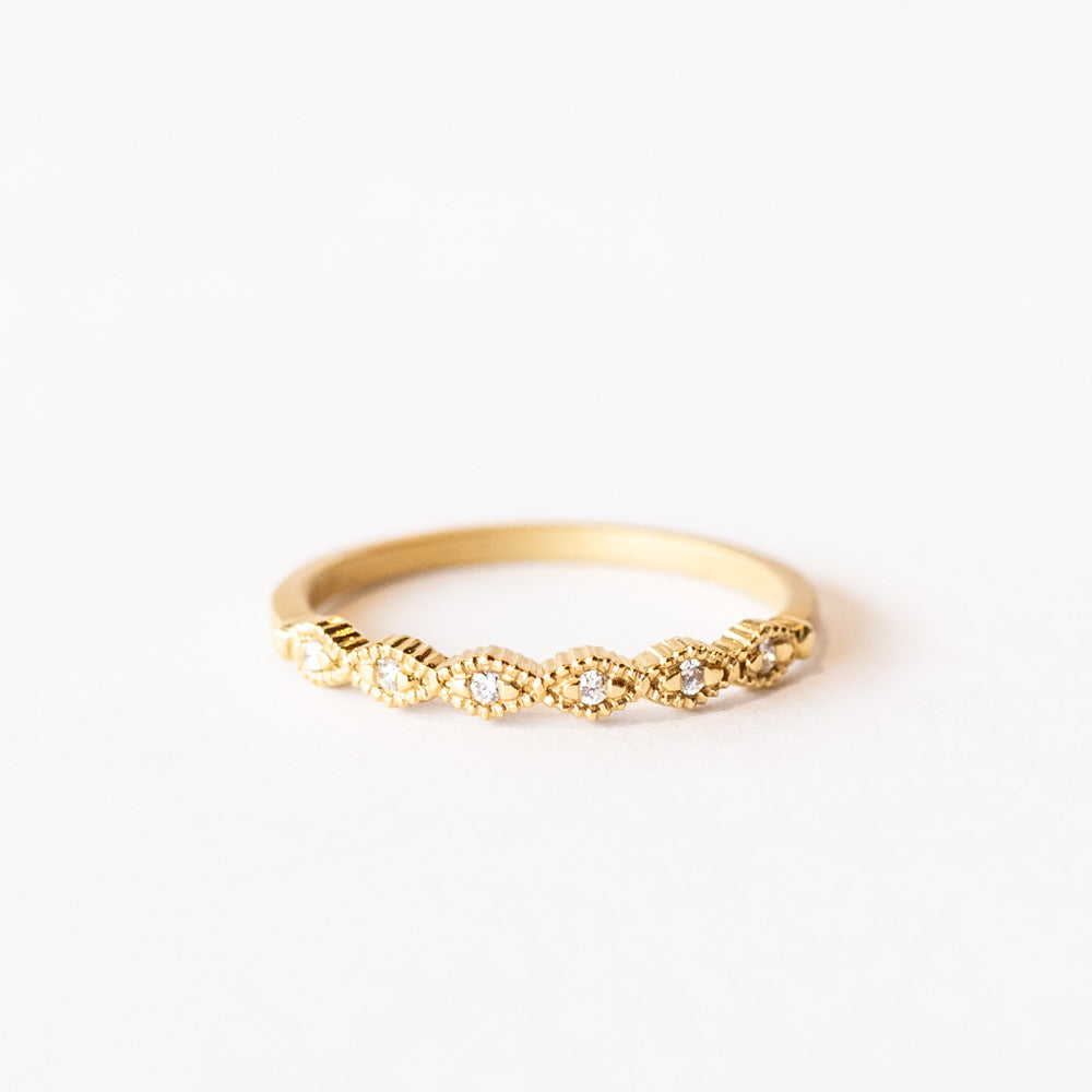 A slender yellow gold wedding band featuring carved diamond shapes across the top set with tiny diamonds and edged with milgrain beading.