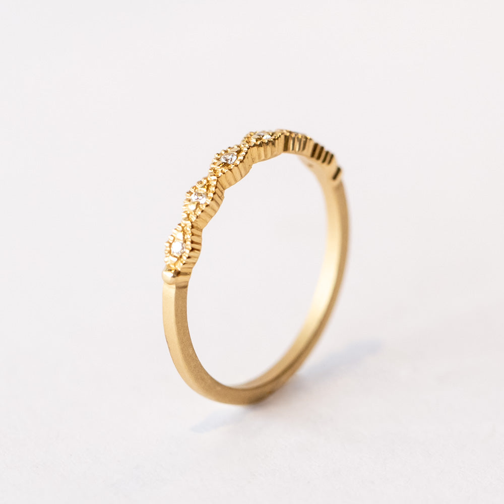 A slender yellow gold wedding band featuring carved diamond shapes across the top set with tiny diamonds and edged with milgrain beading.