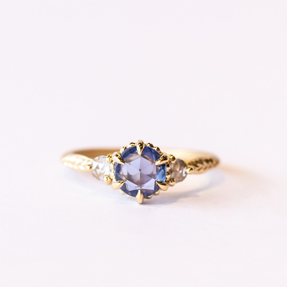 A yellow gold three-stone engagement ring with a rose cut blue sapphire flanked by two rose cut white diamonds.