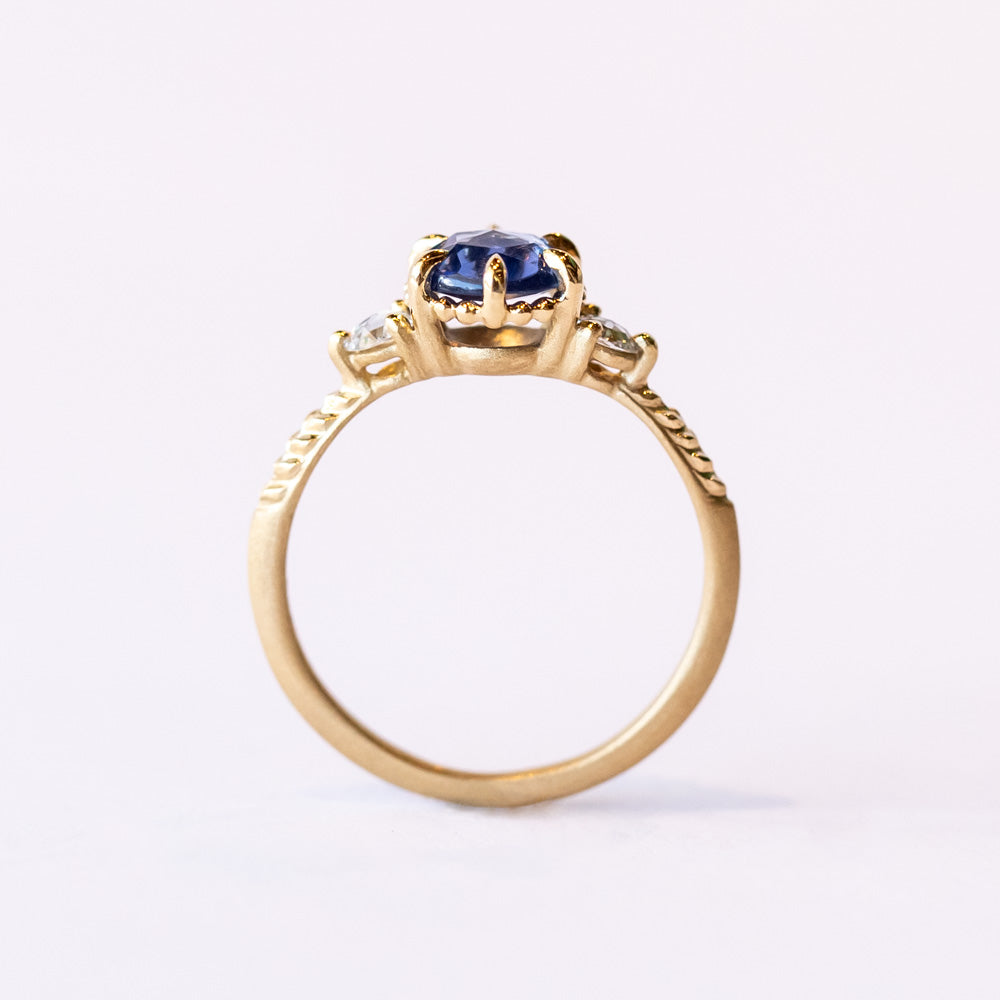 A yellow gold three-stone engagement ring with a rose cut blue sapphire flanked by two rose cut white diamonds.
