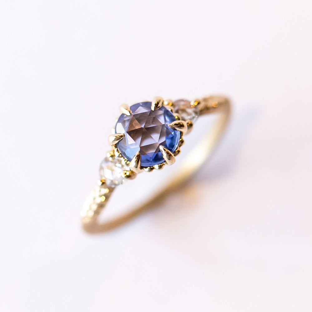 A yellow gold three-stone engagement ring with a rose cut blue sapphire flanked by two rose cut white diamonds.
