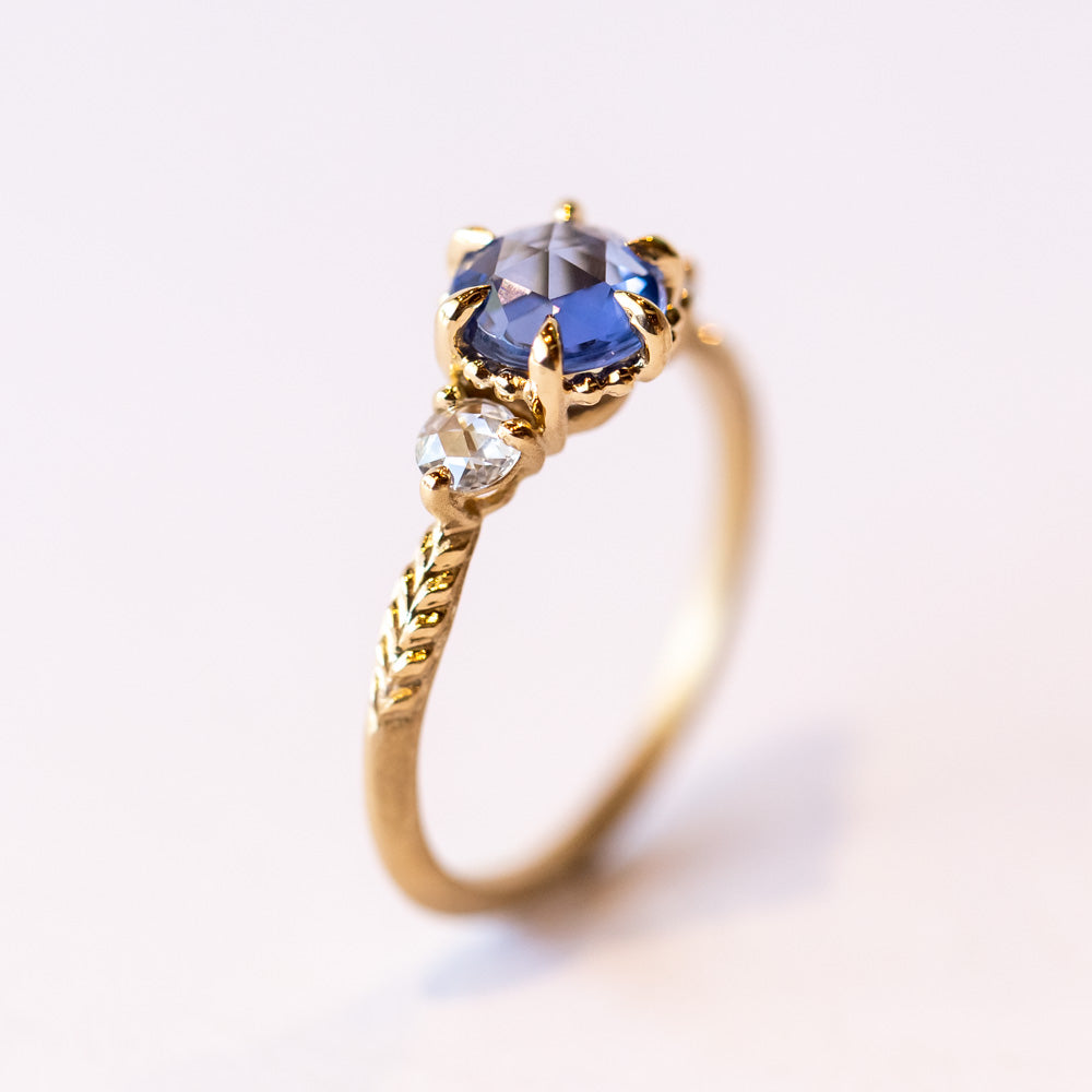 A yellow gold three-stone engagement ring with a rose cut blue sapphire flanked by two rose cut white diamonds.