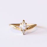 A unique yellow gold engagement ring featuring a peaked design set with an asymmetrical diamond paring of a pear shape rose cut with a tiny round diamond. Leaf accents adorn each shoulder.