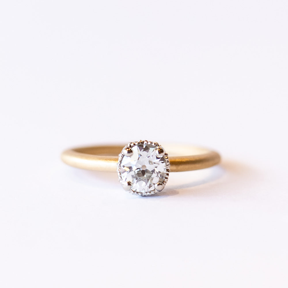 A yellow gold solitaire engagement ring with a white gold center head featuring an old European cut diamond. The sides of the center basket are set with tiny diamonds in milgrain details.