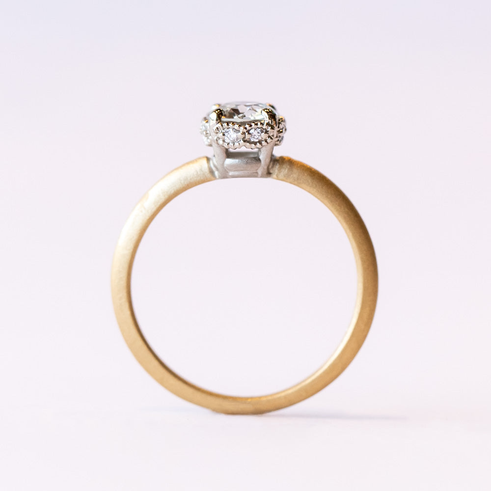 A yellow gold solitaire engagement ring with a white gold center head featuring an old European cut diamond. The sides of the center basket are set with tiny diamonds in milgrain details.
