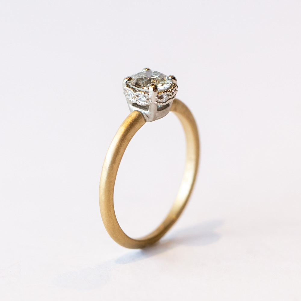 A yellow gold solitaire engagement ring with a white gold center head featuring an old European cut diamond. The sides of the center basket are set with tiny diamonds in milgrain details.