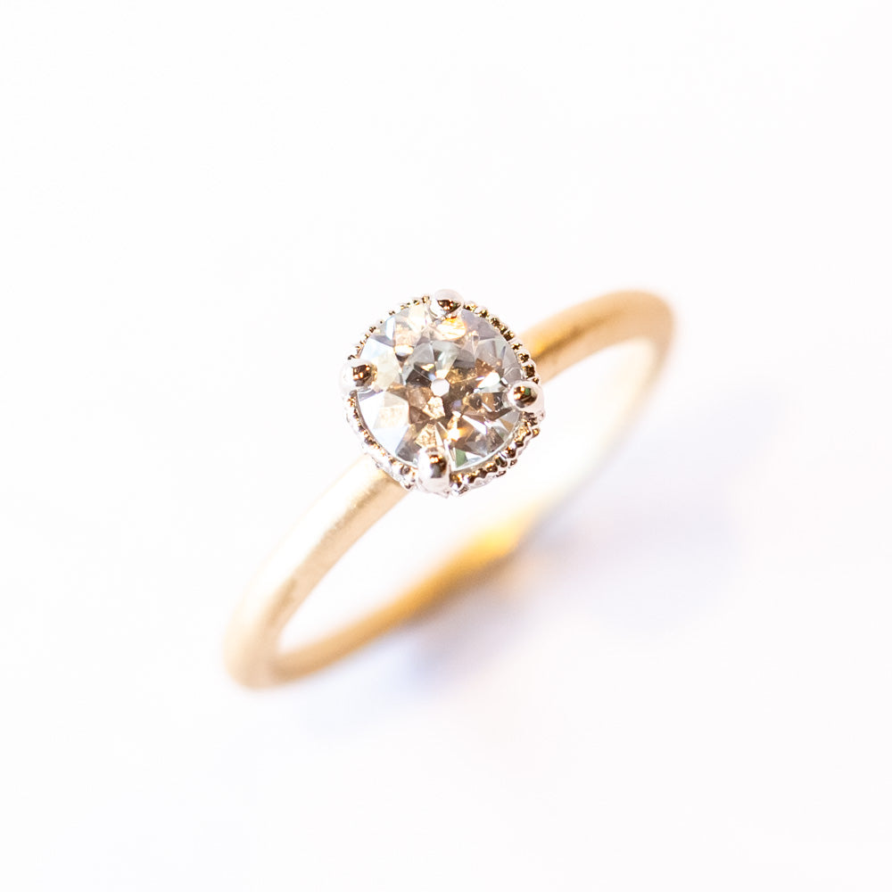 A yellow gold solitaire engagement ring with a white gold center head featuring an old European cut diamond. The sides of the center basket are set with tiny diamonds in milgrain details.
