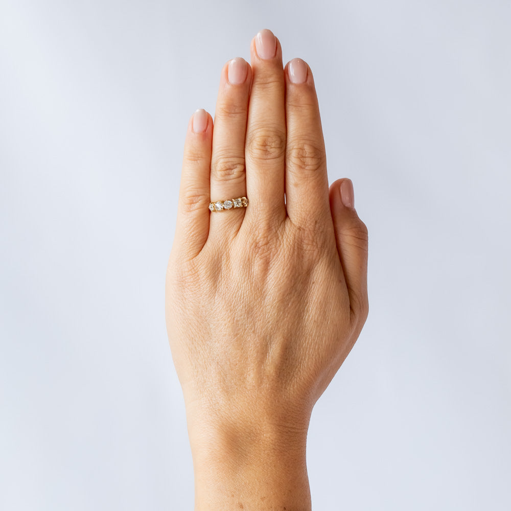 A yellow gold wedding band featuring five mixed-cut diamonds prong set with leaf-like accents on each side. On hand.