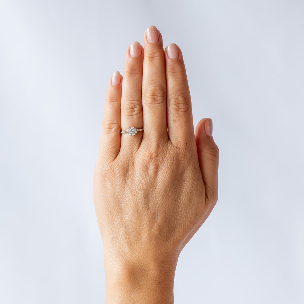 An old mine cut diamond is prong set into a 6-claw solitaire setting in white gold. The slender band has carved foliage motif on either side of the diamond. On hand.