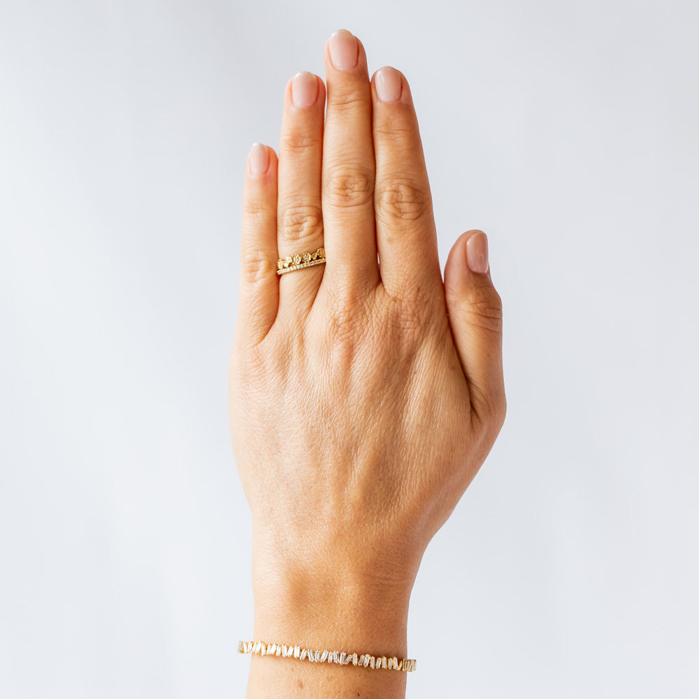 A yellow gold band with a slender row of diamonds topped with a floral tiara on one side. The small flowers and leaves are dotted with additional diamonds. On hand.