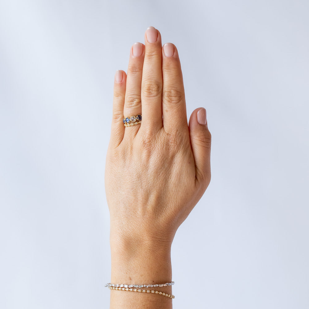 A yellow gold band set with three rose cut blue sapphires and one rose cut diamond. There are tiny white diamonds in between each stone and the settings are edged with bead details. On hand.
