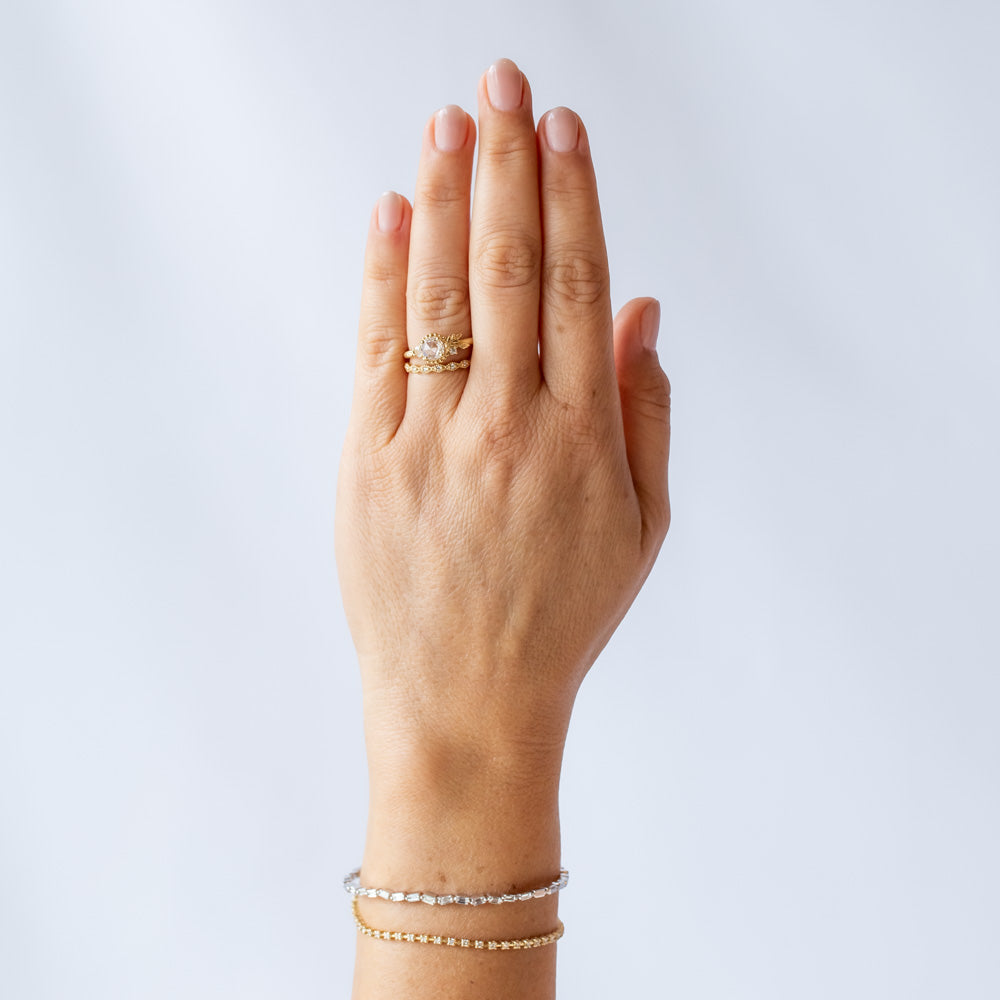 A yellow gold engagement ring with a round, rose cut center diamond accented by asymmetrical foliate elements and two small side diamonds. On hand.