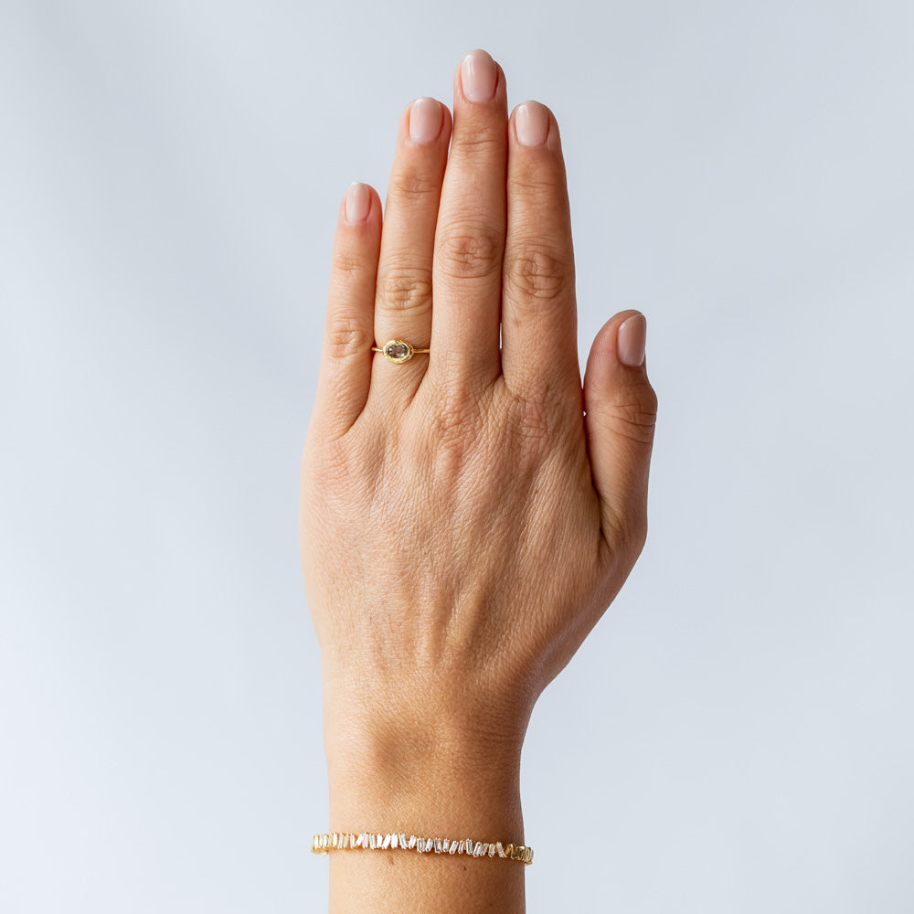 An oval rose cut green sapphire is bezel set into a textured yellow gold ring. On hand.