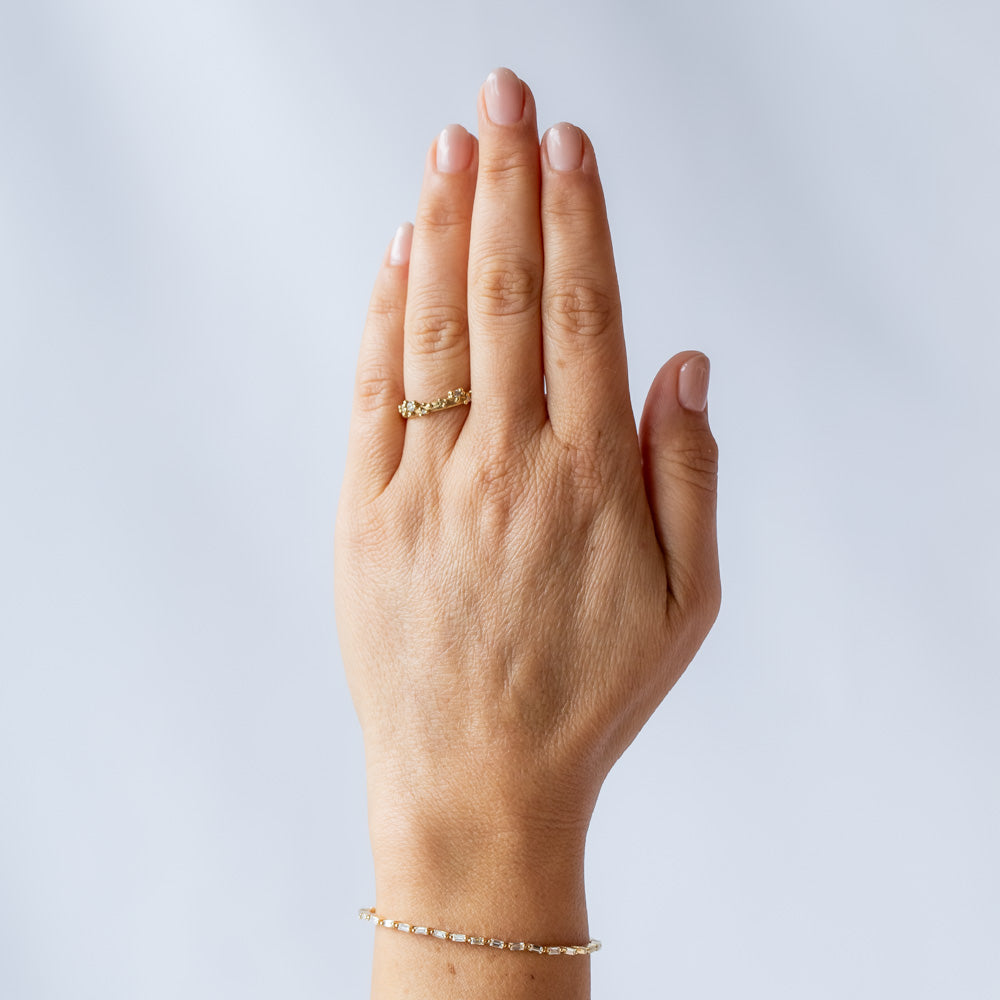 A stackable band featuring five white diamonds nestling amongst granules of yellow gold on a gently textured half round band. On hand.