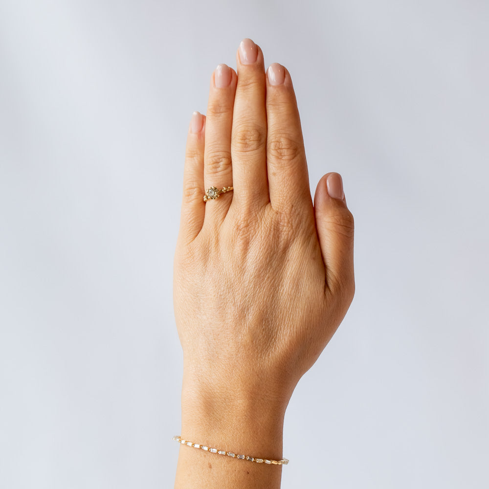 A round diamond solitaire engagement ring set in a granulated setting in yellow gold. On hand.