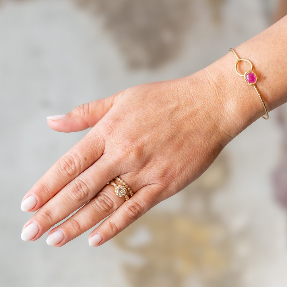 A yellow gold wire bracelet set with a bezel set ruby at one end that fits through a loop at the other. On model.