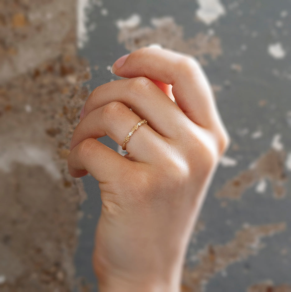 A lauren-wreath patterned wedding band in yellow gold with three accent diamonds. On hand.