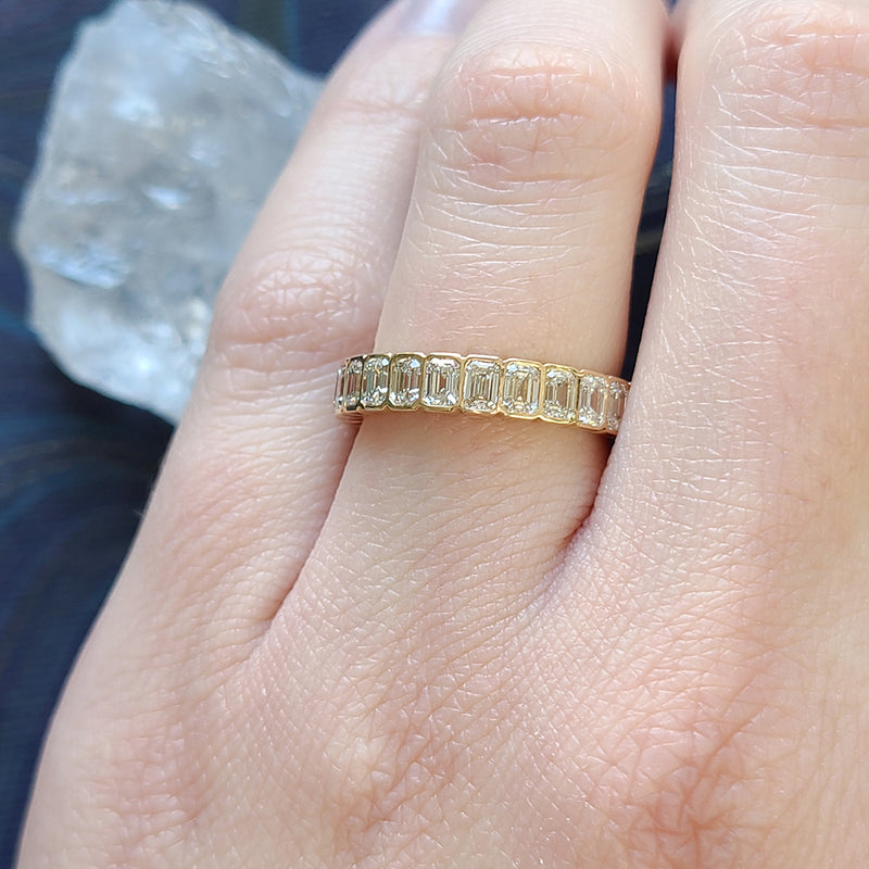 A yellow gold and diamond eternity band with bezel set emerald cut diamonds set vertically all the way around. On hand.