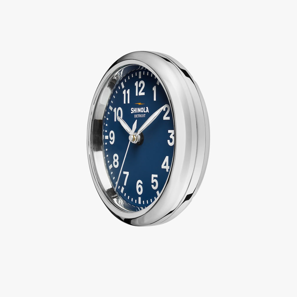 round Shinola desk clock with wooden stand, navy face and chrome rim with white hands