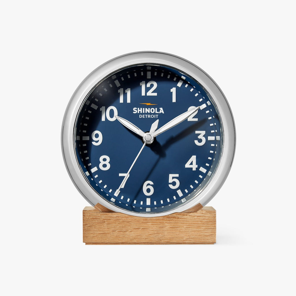 round Shinola desk clock with wooden stand, navy face and chrome rim with white hands