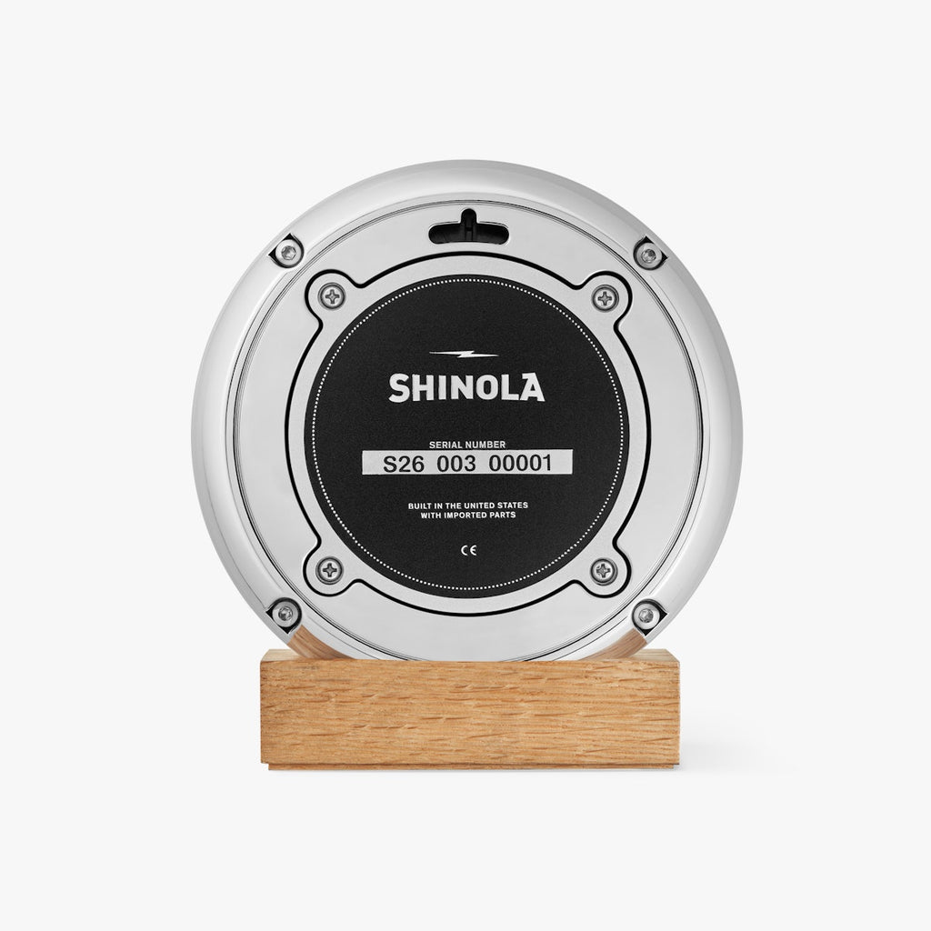 round Shinola desk clock with wooden stand, navy face and chrome rim with white hands