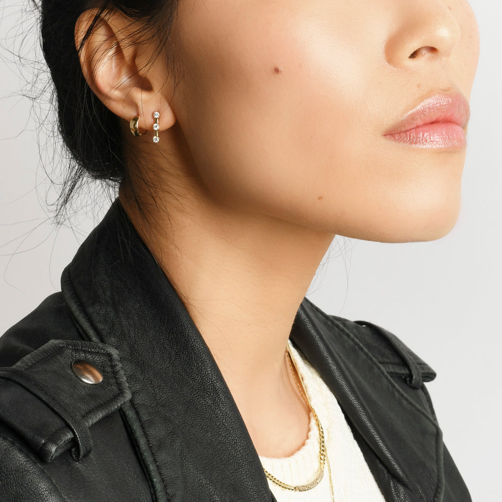 Earrings made of three prong set round diamonds spaced out by flexible gold bars in between. On model.