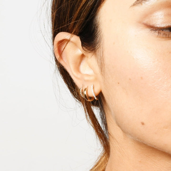 A petite gold hoop earring with a row of round pave set diamonds down the front. On model.