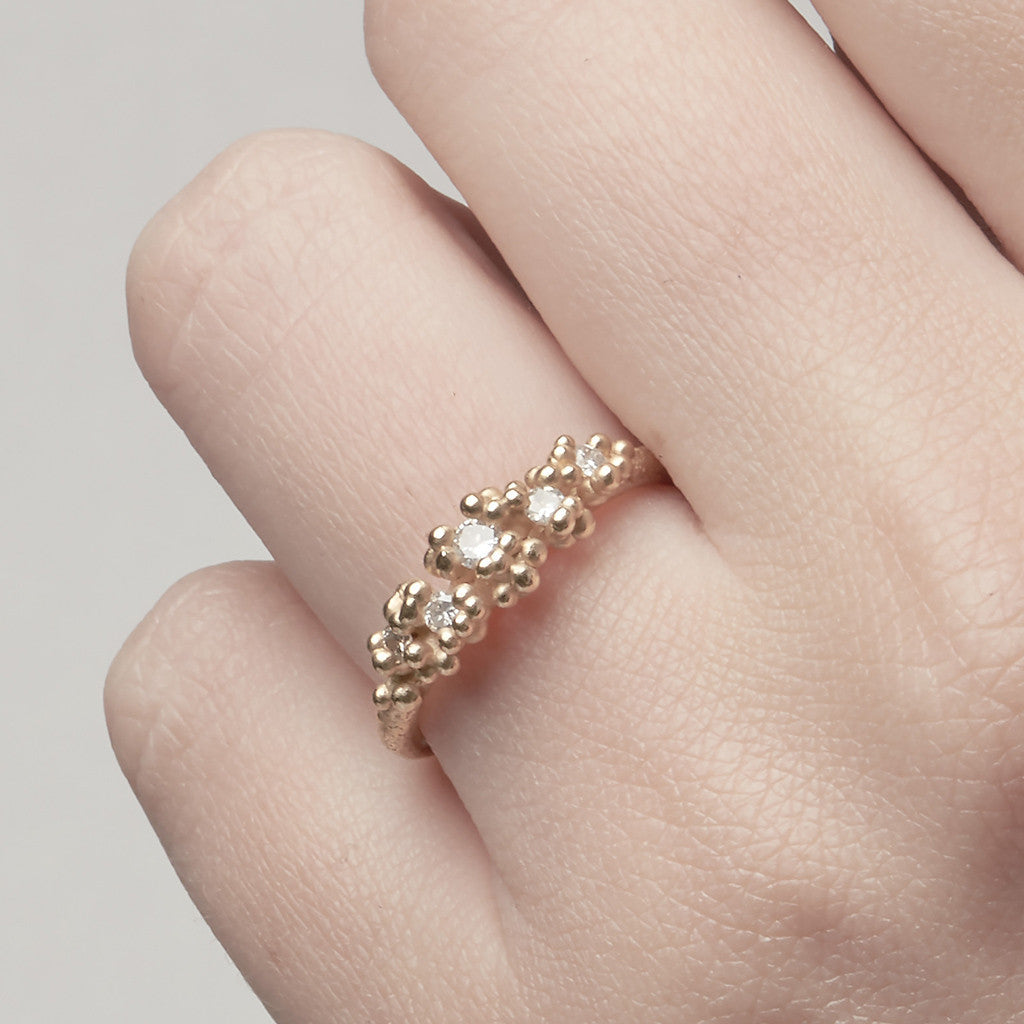 Unique diamond cluster engagement ring with golden granules, on a gently textured band.
