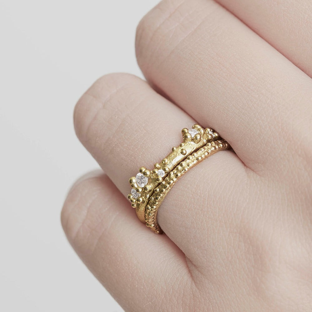 A stackable band featuring five white diamonds nestling amongst granules of yellow gold on a gently textured half round band. On hand