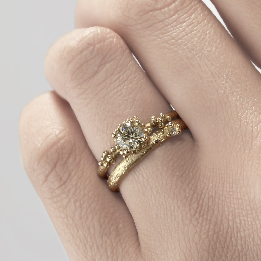 A textured yellow gold band with one tiny diamond set in gold granules. On hand.