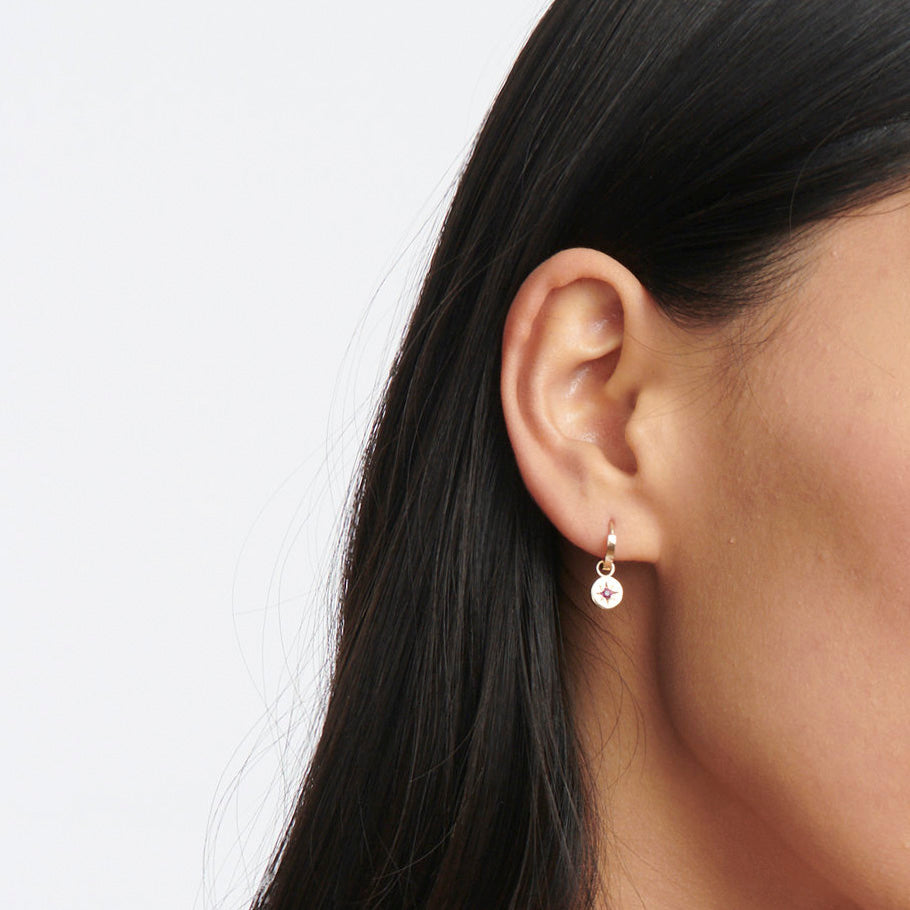 Dainty gold circle drops with a star-set aquamarine gemstone hang from small gold huggie hoop earrings.