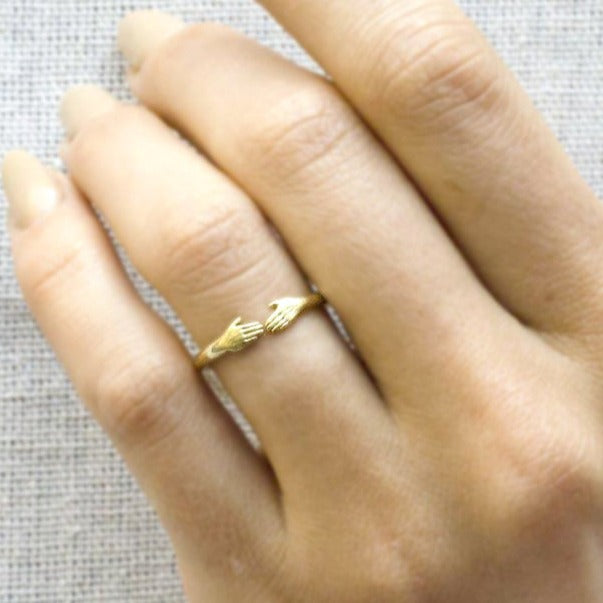 A dainty gold Anthony Lent ring featuring two tiny hands facing each other at the center. On model view.