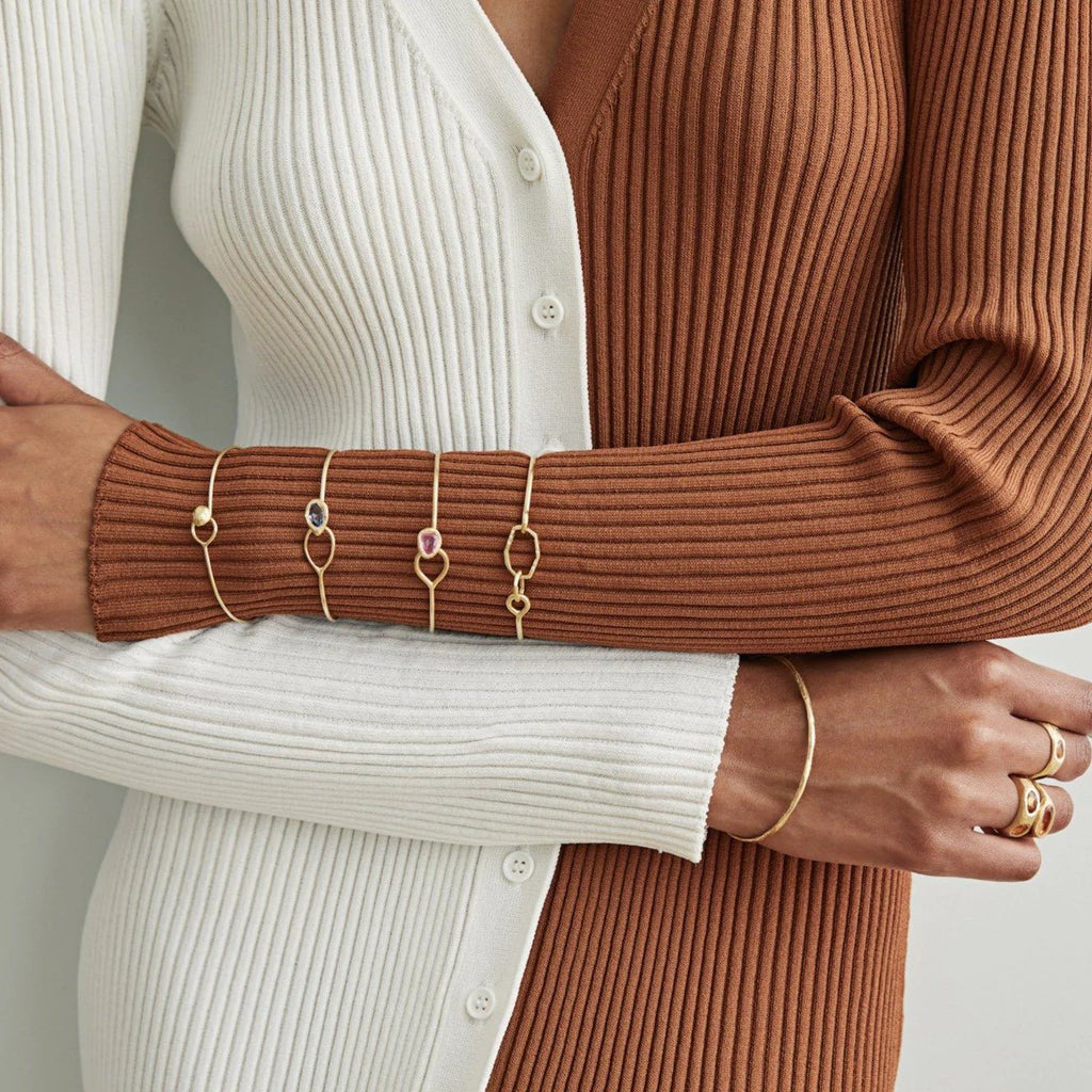 A yellow gold wire bracelet set with a bezel set ruby at one end that fits through a loop at the other. Model shot.