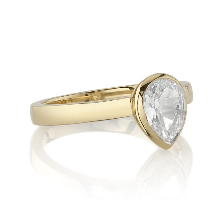 A pear-shaped diamond is bezel set in yellow gold on a solitaire engagement ring.