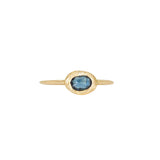 A slender, textured yellow gold ring with an east-west, bezel set teal blue sapphire.