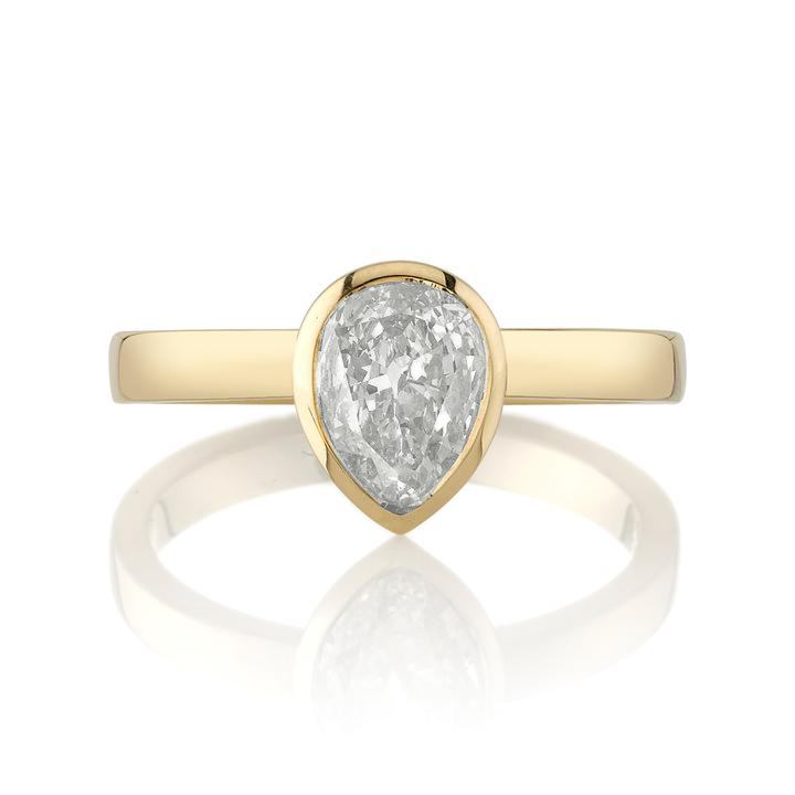A pear-shaped diamond is bezel set in yellow gold on a solitaire engagement ring.