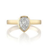 A pear-shaped diamond is bezel set in yellow gold on a solitaire engagement ring.