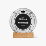 Shinola red desk clock with silver case, sitting on a tan wooden block, back view