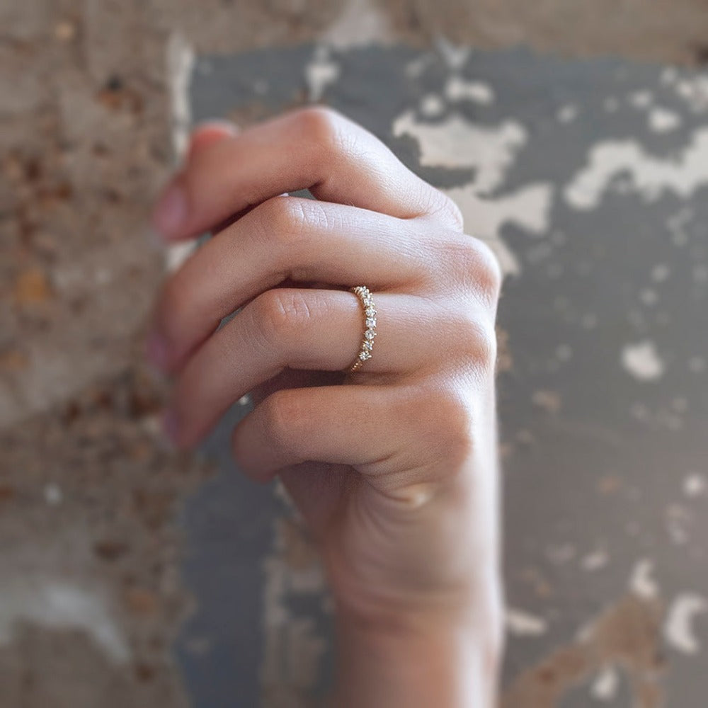 A yellow gold band featuring a row of 9 single-cut white diamonds set with alternating direction prongs. On hand.