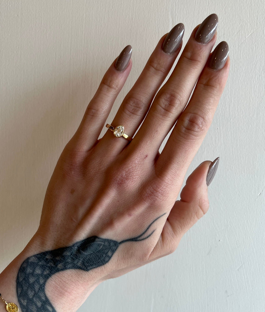 A pear-shaped diamond is bezel set in yellow gold on a solitaire engagement ring. On model.